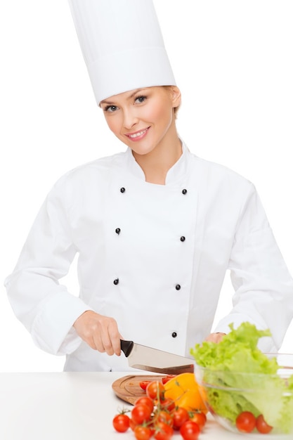 koncepcja gotowania i jedzenia - uśmiechnięta kobieta szef kuchni sieka warzywa