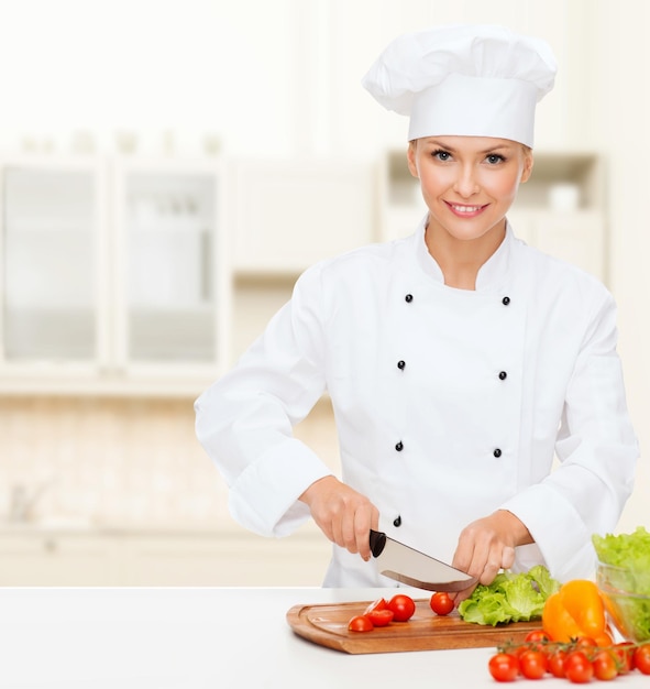 koncepcja gotowania i jedzenia - uśmiechnięta szefowa kuchni, kucharz lub piekarz siekający warzywa