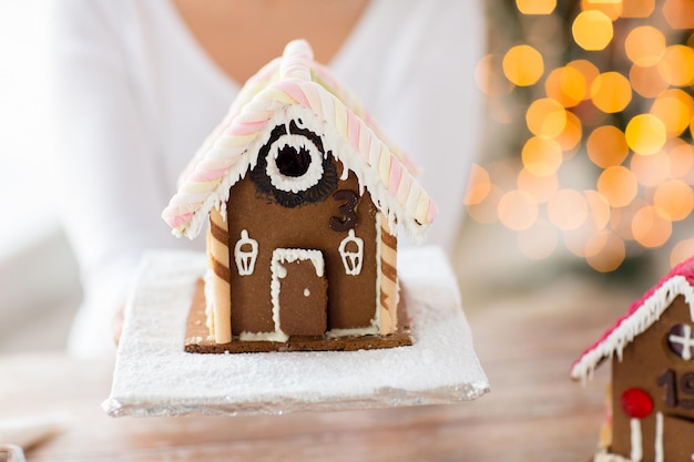 koncepcja gotowania, ludzi, świąt i pieczenia - zbliżenie szczęśliwej kobiety trzymającej i pokazującej piernikowy dom w domu