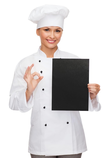 koncepcja gotowania, reklamy i jedzenia - uśmiechnięta szefowa kuchni, kucharz lub piekarz z czystym czarnym papierem pokazującym ok śpiewa