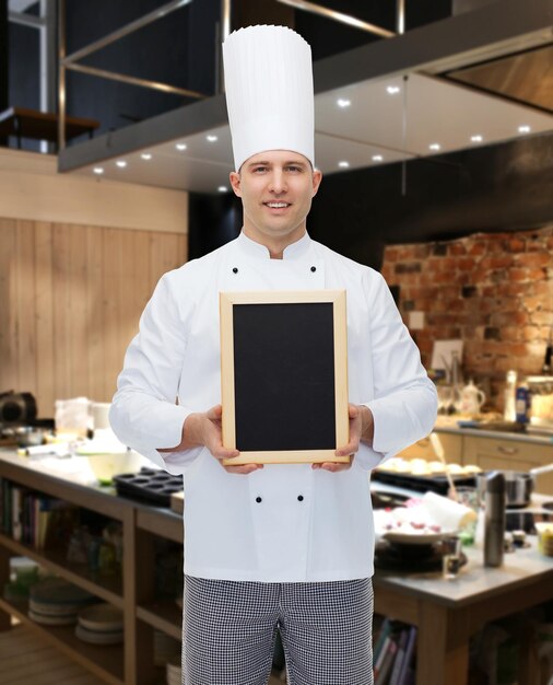 Koncepcja Gotowania, Zawodu, Reklamy I Ludzi - Szczęśliwy Kucharz Mężczyzna Pokazujący I Trzymający Pustą Tablicę Menu Nad Kuchnią Restauracji