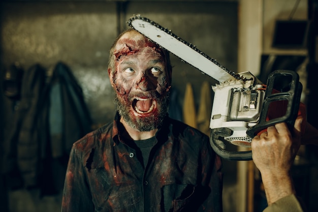 Zdjęcie koncepcja halloween obrony zombie i piłą łańcuchową. makijaż skóry i zakrwawionej twarzy