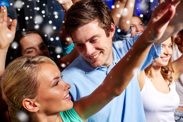 koncepcja imprez, wakacji, uroczystości, życia nocnego i ludzi - uśmiechnięci przyjaciele machający rękami na koncercie w klubie i efekt śniegu