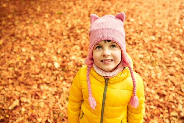 koncepcja jesień, dzieciństwo, natura i ludzie - szczęśliwa mała dziewczynka nad opadłymi liśćmi w parku