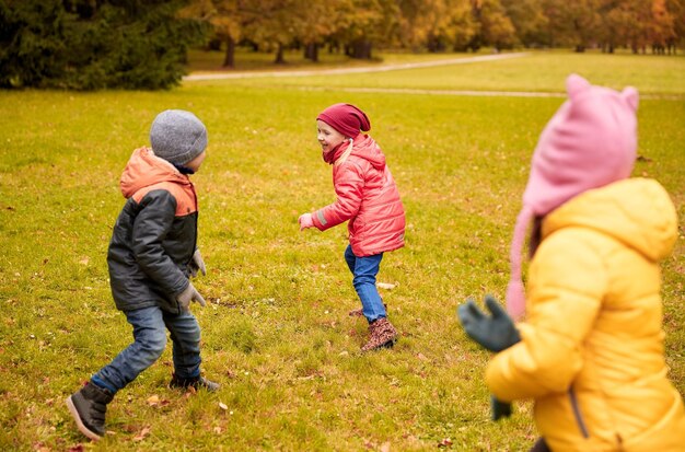 koncepcja jesień, dzieciństwo, wypoczynek i ludzie - grupa szczęśliwych małych dzieci grających w tag game i biegających w parku na świeżym powietrzu