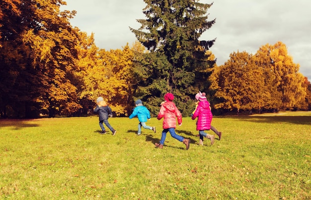 koncepcja jesień, dzieciństwo, wypoczynek i ludzie - grupa szczęśliwych małych dzieci grających w tag game i biegających w parku na świeżym powietrzu