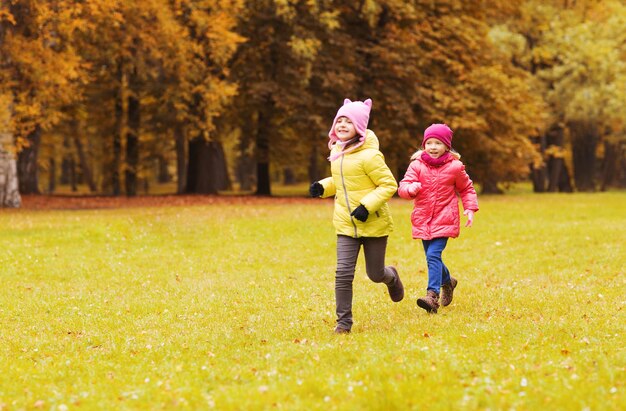 koncepcja jesień, dzieciństwo, wypoczynek i ludzie - szczęśliwe małe dziewczynki grają w tag game i biegają w parku na świeżym powietrzu