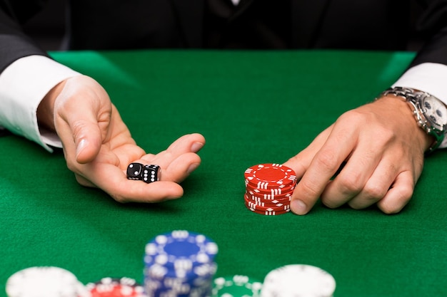 koncepcja kasyna, hazardu, pokera, ludzi i rozrywki - zbliżenie pokerzysty z kośćmi i żetonami przy zielonym stole w kasynie