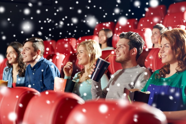 koncepcja kina, rozrywki i ludzi - szczęśliwi przyjaciele z popcornem i lemoniadą oglądając film w teatrze z płatkami śniegu