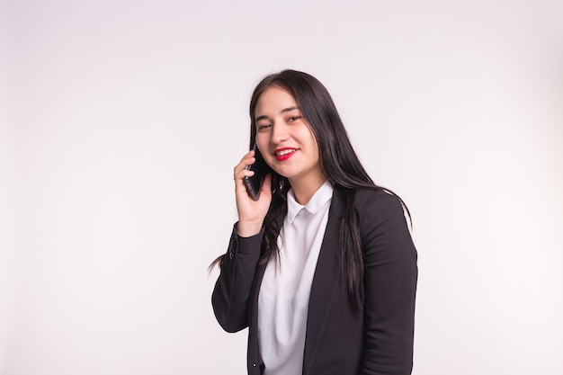 Koncepcja komunikacji i ludzi. młoda kobieta brunetka rozmawia przez telefon komórkowy i uśmiecha się na białym tle z miejsca na kopię