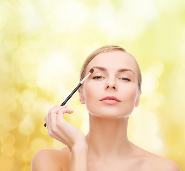 koncepcja kosmetyków, zdrowia i urody - piękna kobieta z pędzlem do makijażu