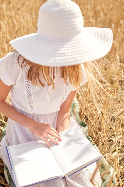 koncepcja kraju, letnich wakacji, literatury i ludzi - zbliżenie młodej kobiety w białym słomkowym kapeluszu i sukience czytającej książkę na polu zbóż