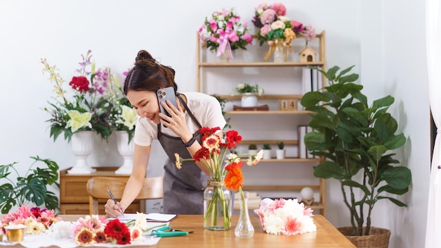 Koncepcja kwiaciarni Kobieta kwiaciarnia rozmawia z klientem na smartfonie i robi notatkę na notebooku