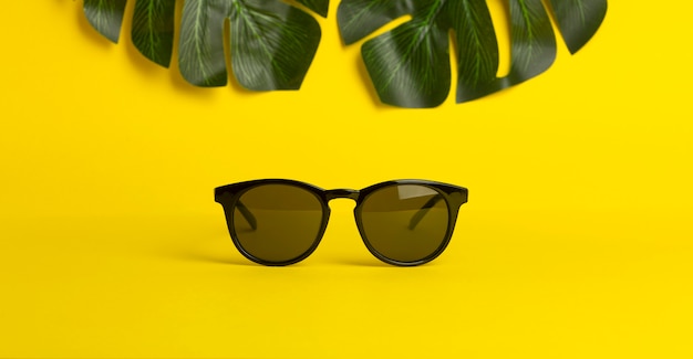Koncepcja lato i wakacje. Okulary przeciwsłoneczni i tropikalni liście na żółtym barwionym tle
