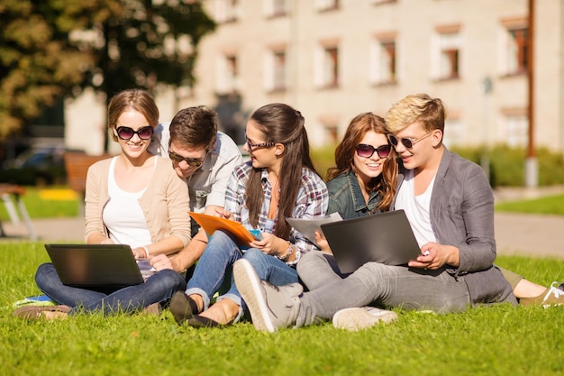 koncepcja lato, internet, edukacja, kampus i młodzież - grupa studentów lub nastolatków z laptopem, zeszytami, plikami i folderami