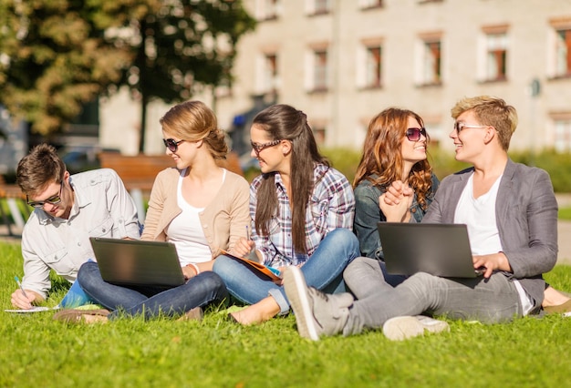 koncepcja lato, internet, edukacja, technologia i kampus - grupa studentów lub nastolatków z laptopem, zeszytami, plikami i folderami