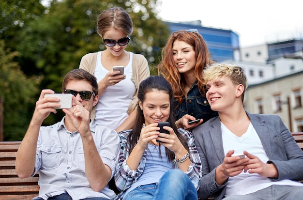 koncepcja lato, technologia, edukacja i młodzież - grupa szczęśliwych studentów lub nastolatków ze smartfonami biorącymi selfie i wysyłających wiadomości tekstowe w kampusie