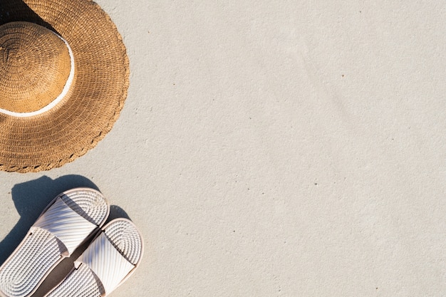 Koncepcja letnich wakacji: kapcie plażowe i kapelusz na czystym piasku. Widok z góry akcesoriów na wakacje nad morzem z naturalną przestrzenią przypominającą wybrzeże