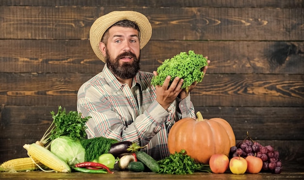 Koncepcja lokalnie uprawianych upraw Kup warzywa Lokalna farma Typowy farmer Targowisko dożynkowe Mężczyzna dojrzały brodaty rolnik trzymaj warzywa na drewnianym tle Sprzedawaj warzywa Lokalny rynek