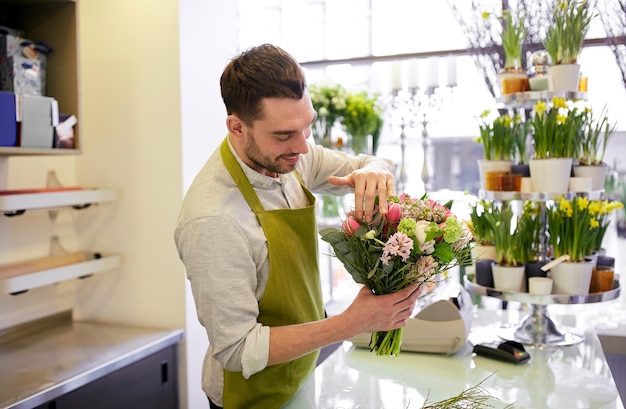 koncepcja ludzi, biznesu, sprzedaży i florystyki - szczęśliwy uśmiechnięty mężczyzna kwiaciarnia robi wiązkę w kwiaciarni