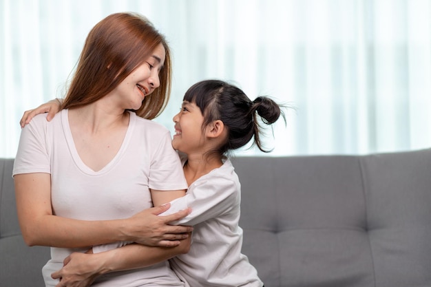 Koncepcja ludzi i rodziny - szczęśliwa uśmiechnięta dziewczyna z matką przytulającą się na kanapie w domu