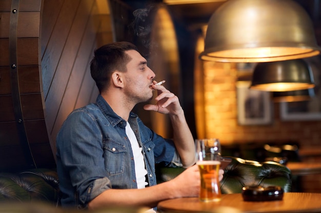 koncepcja ludzi i złych nawyków - mężczyzna pijący piwo i palący papierosy w barze lub pubie