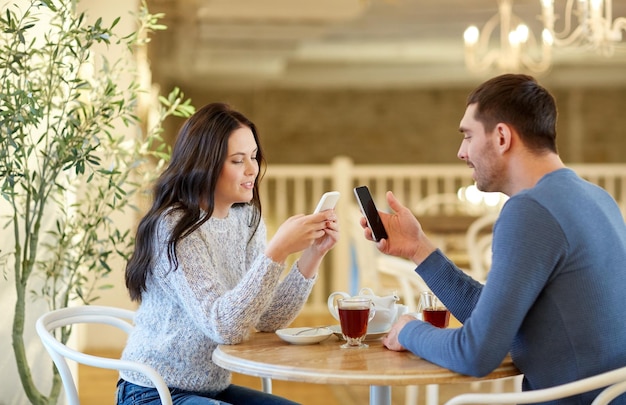 koncepcja ludzi, komunikacji i randek - szczęśliwa para ze smartfonami pijąca herbatę w kawiarni lub restauracji