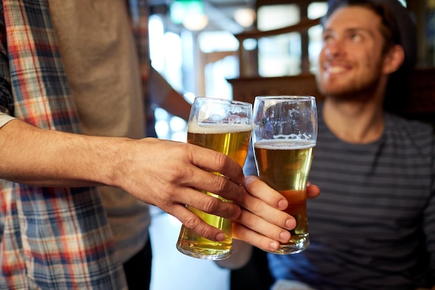 Koncepcja ludzi, mężczyzn, czasu wolnego, przyjaźni i świętowania - szczęśliwi przyjaciele płci męskiej popijający piwo i brzęczący szklankami w barze lub pubie