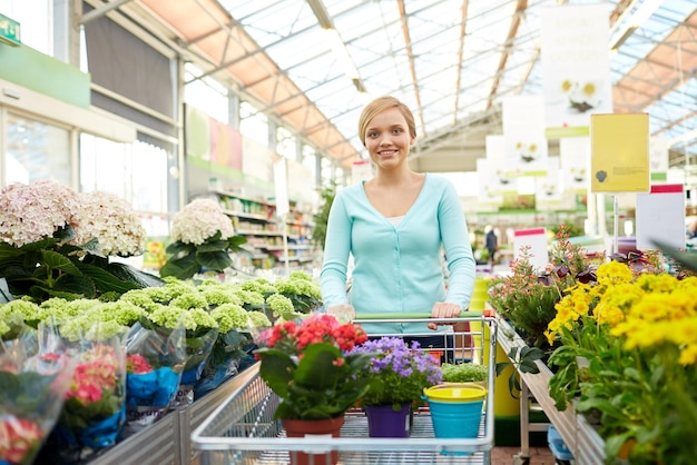koncepcja ludzi, ogrodnictwa, sprzedaży i konsumpcjonizmu - szczęśliwa kobieta z koszykiem i kwiatami w sklepie lub szklarni