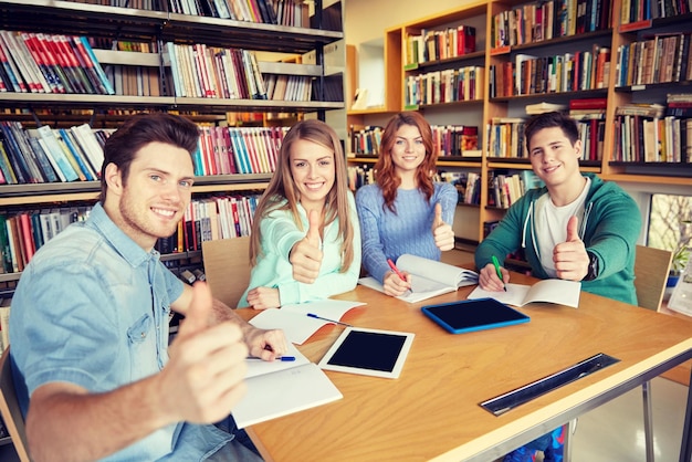 koncepcja ludzi, wiedzy, edukacji i szkoły - grupa szczęśliwych uczniów z komputerami typu tablet PC pokazującymi aprobaty w bibliotece