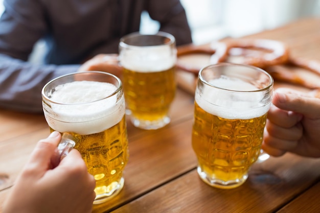 koncepcja ludzi, wypoczynku i napojów - zbliżenie męskich rąk brzęczących kuflami piwa w barze lub pubie