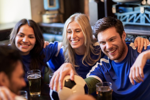 Zdjęcie koncepcja ludzi, wypoczynku, piłki nożnej i sportu - szczęśliwi fani piłki nożnej lub przyjaciele z piwem i piłką świętują zwycięstwo w barze lub pubie