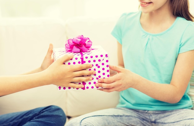koncepcja ludzie, dzieci, święta, przyjaciele i przyjaźń - zbliżenie szczęśliwych dziewczynek z prezentem urodzinowym siedzących na kanapie w domu