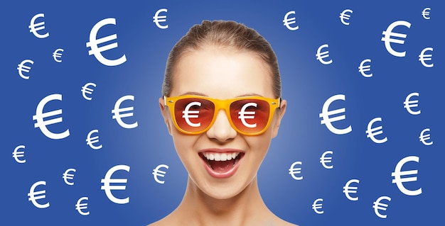 Zdjęcie koncepcja ludzie, finanse i pieniądze - szczęśliwa krzycząca nastolatka w odcieniach na niebieskim tle ze śpiewami waluty euro