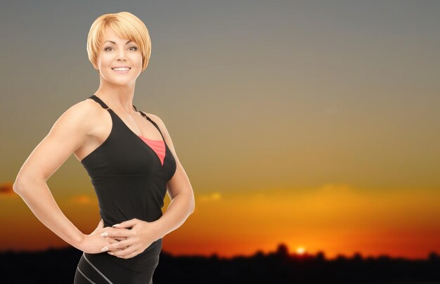 koncepcja ludzie, fitness i sport - szczęśliwa kobieta pozuje na zewnątrz na tle panoramy zachodu słońca