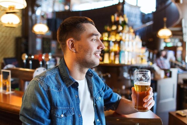 koncepcja ludzie, napoje, alkohol i wypoczynek - szczęśliwy młody człowiek pijący piwo w barze lub pubie