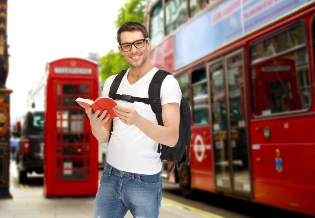 koncepcja ludzie, podróże, turystyka i edukacja - szczęśliwy młody człowiek z plecakiem i książką nad autobusem miejskim w Londynie na tle ulicy