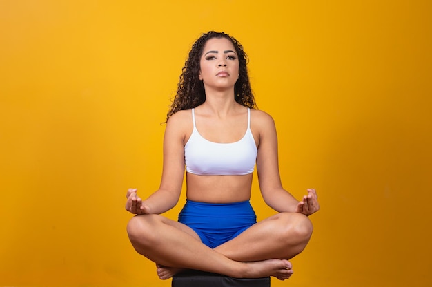 Koncepcja ludzie, pokój i medytacja. Spokojna afro młoda kobieta praktykuje jogę na żółtym tle.