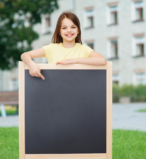 koncepcja ludzie, reklama i edukacja - szczęśliwa mała dziewczynka wskazująca palcem na tablicę