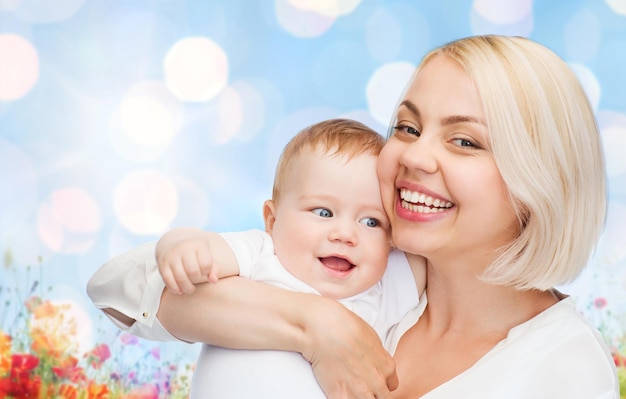 koncepcja ludzie, rodzina, macierzyństwo i dzieci - szczęśliwa matka przytulająca urocze dziecko nad niebieskimi światłami i tłem pola makowego