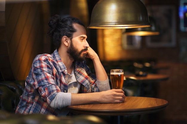 koncepcja ludzie, samotność, alkohol i styl życia - nieszczęśliwy samotny mężczyzna z brodą pijący piwo w barze lub pubie