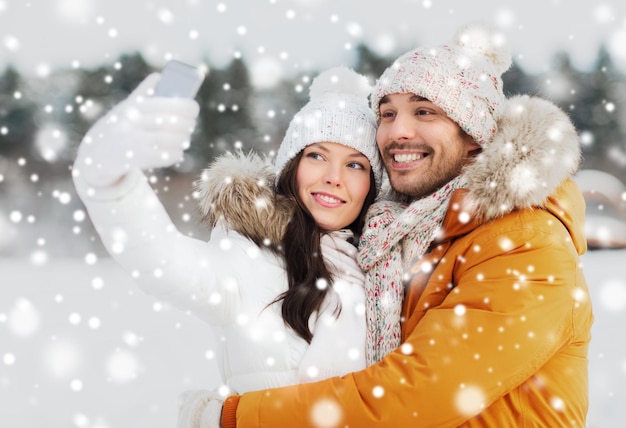 Koncepcja ludzie, sezon, miłość, technologia i wypoczynek - szczęśliwa para biorąca selfie przez smartfona na tle zimowych