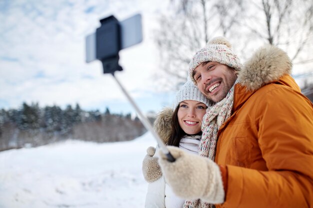 Koncepcja ludzie, sezon, miłość, technologia i wypoczynek - szczęśliwa para robi zdjęcie z selfie smartfona trzymanym na zimowym tle