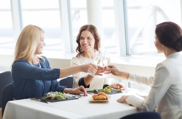 koncepcja ludzie, święta, uroczystości i styl życia - szczęśliwe kobiety pijące szampana i brzękające kieliszki w restauracji