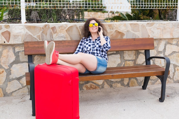 Koncepcja ludzie, wakacje i podróże - młoda kobieta siedzi z nogami na walizce na zewnątrz.