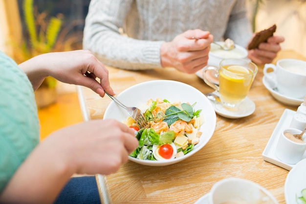 koncepcja ludzie, wypoczynek i jedzenie - bliska przyjaciele jedzący obiad i jedzący w restauracji