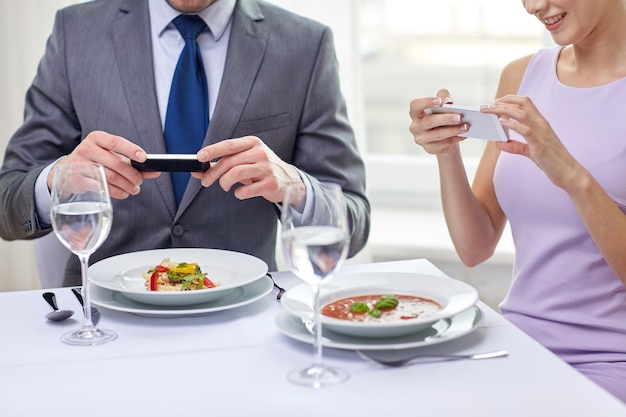 koncepcja ludzie, wypoczynek, jedzenie i technologia - zbliżenie pary ze smartfonami robiącej zdjęcie jedzenia w restauracji