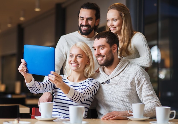 koncepcja ludzie, wypoczynek, technologia i przyjaźń - szczęśliwi przyjaciele z komputerem typu tablet pc biorący selfie w kawiarni