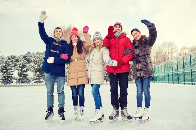 koncepcja ludzie, zima, przyjaźń, sport i wypoczynek - szczęśliwi przyjaciele jeżdżący na łyżwach i machający rękami na lodowisku na świeżym powietrzu