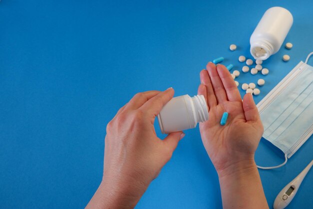 Koncepcja medycyny i opieki zdrowotnej Kobieta wyciąga kapsułkę z pojemnika Kapsułki tabletki maskę medyczną na niebieskim tle Miejsce dla tekstu